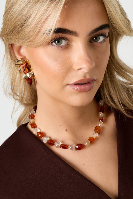 Model wearing amber and white translucent beaded necklace with gold flower earrings and brown top