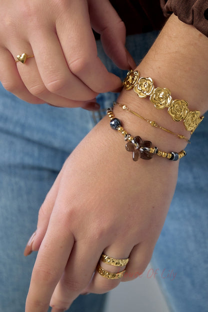 Woman wearing gold floral cuff bracelet along with layered beaded and delicate bracelets; also rings on fingers