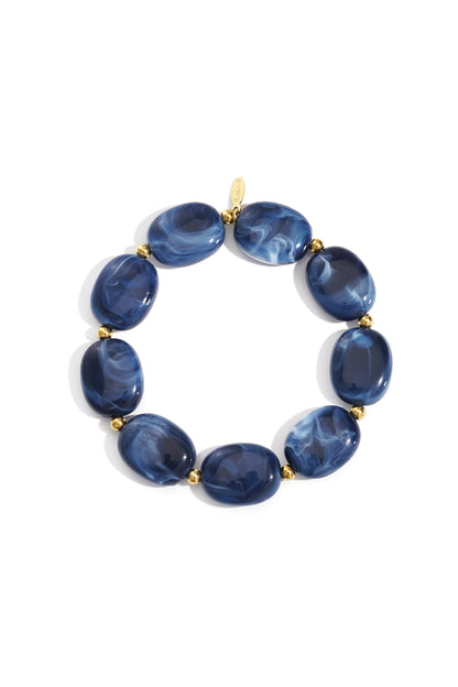 Close-up of a navy blue acrylic beaded bracelet with gold spacers laid flat on white background