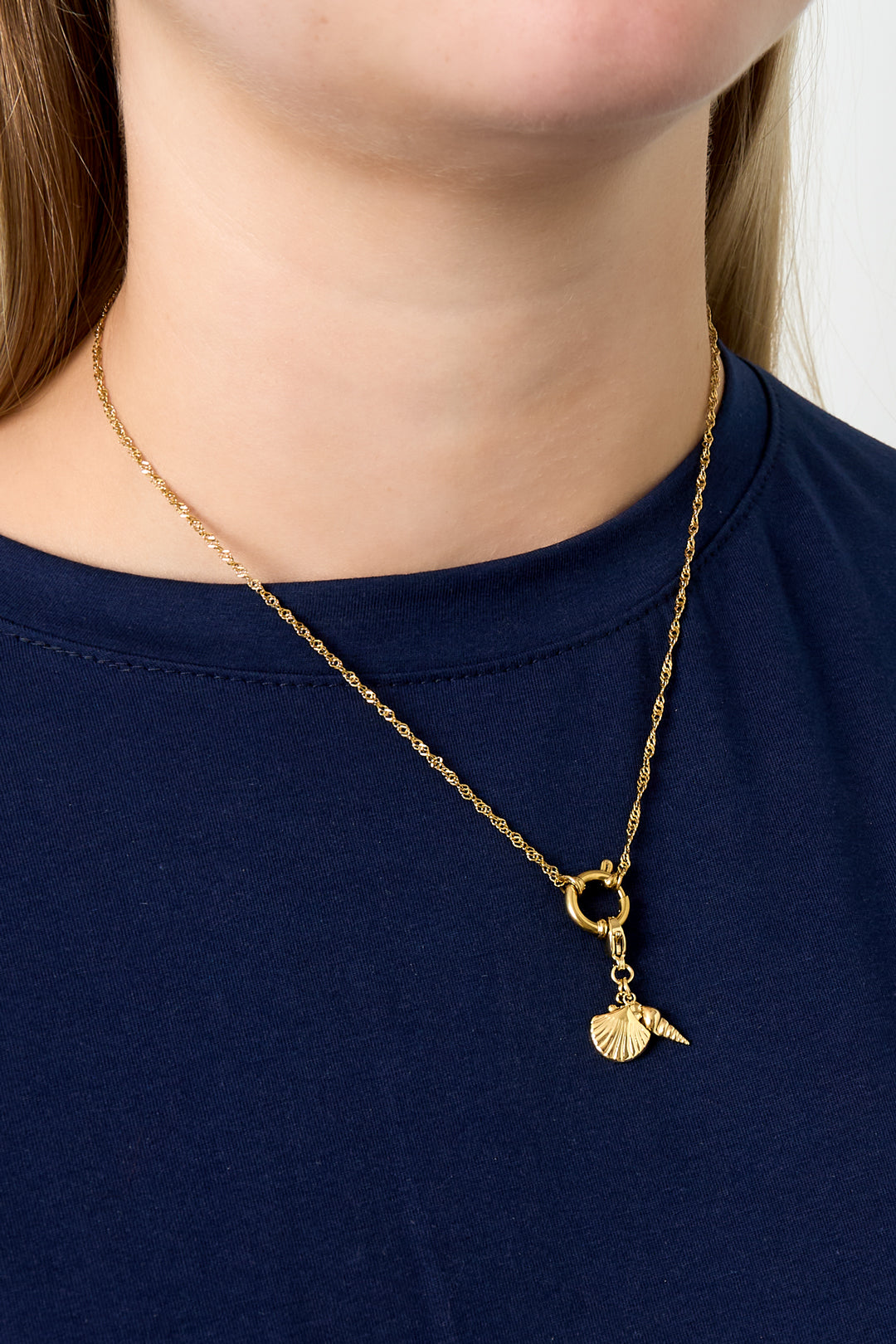 Model wearing gold chain necklace with seashell and spiral shell charms over navy top