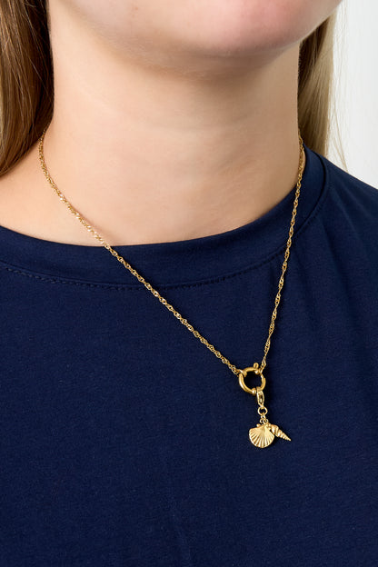 Model wearing gold chain necklace with seashell and spiral shell charms over navy top