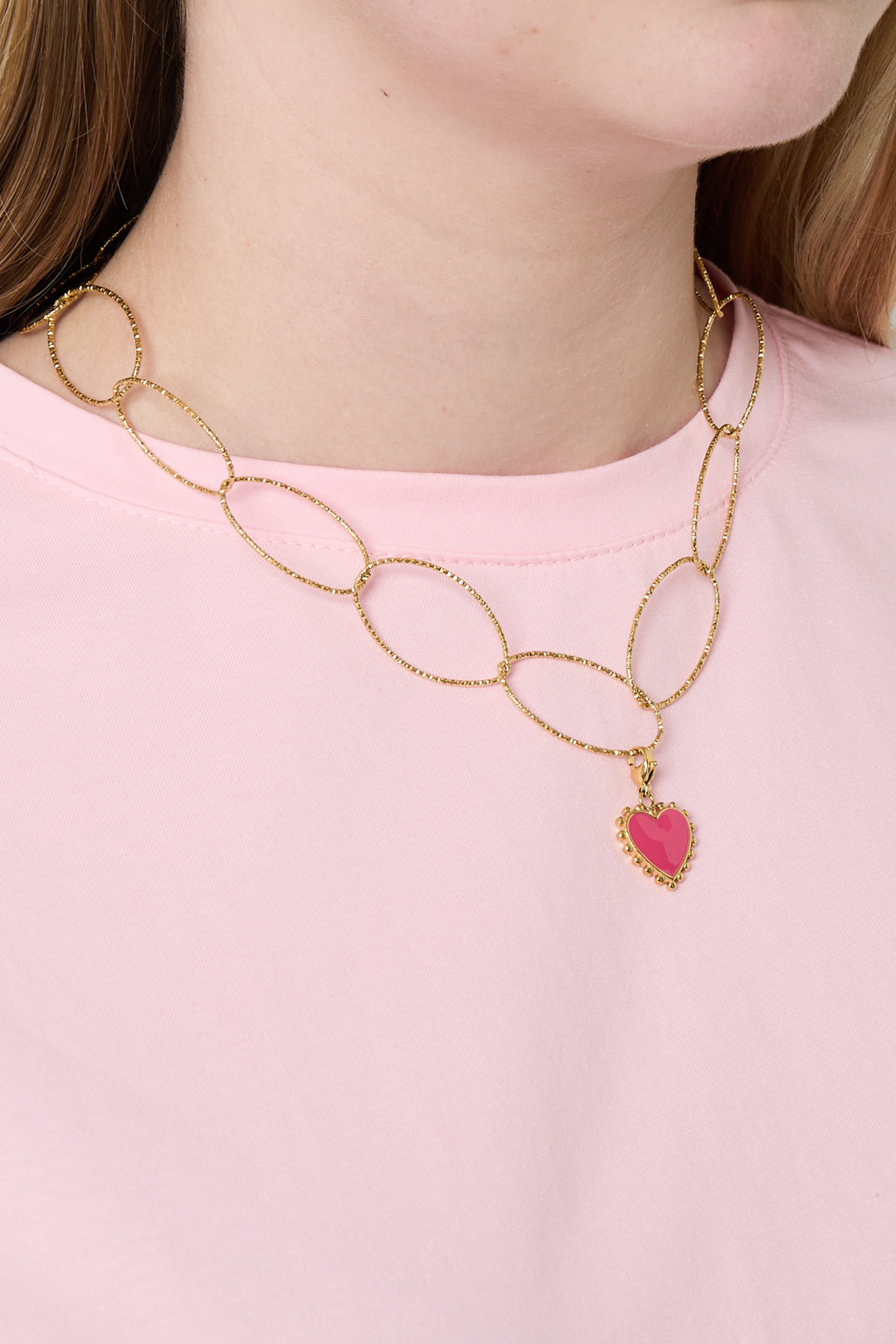 Woman wearing gold chunky oval link necklace with pink heart pendant over light pink shirt