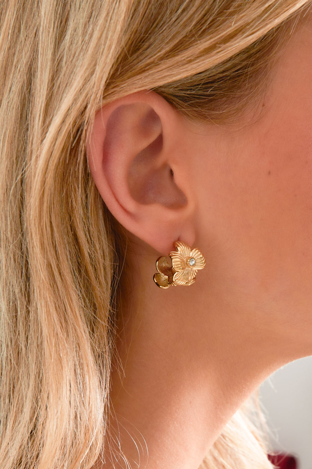Close-up of gold floral hoop earring worn on a woman’s ear, showcasing delicate flower design
