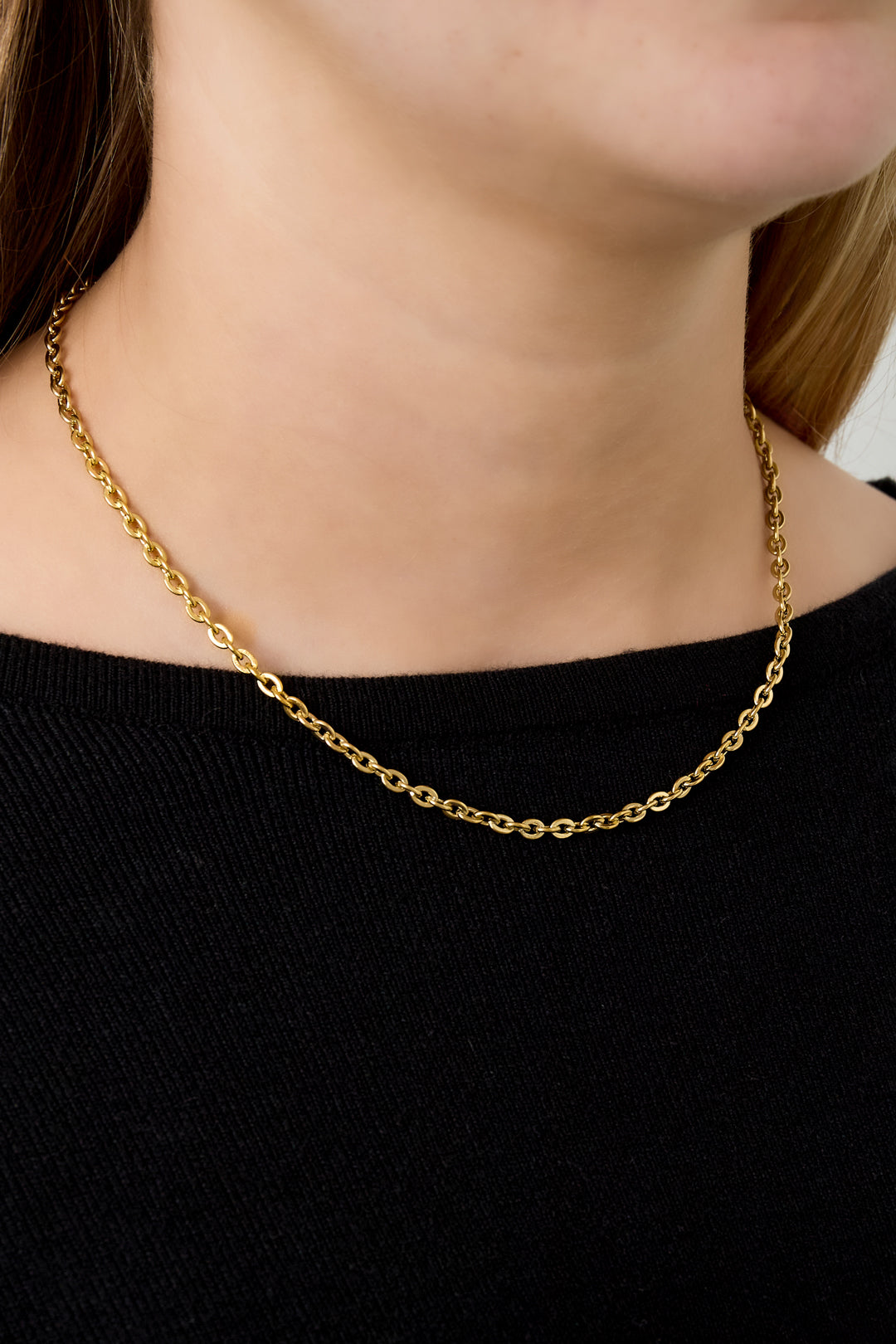 Young woman wearing simple gold chain necklace with black top, showcasing necklace on neck