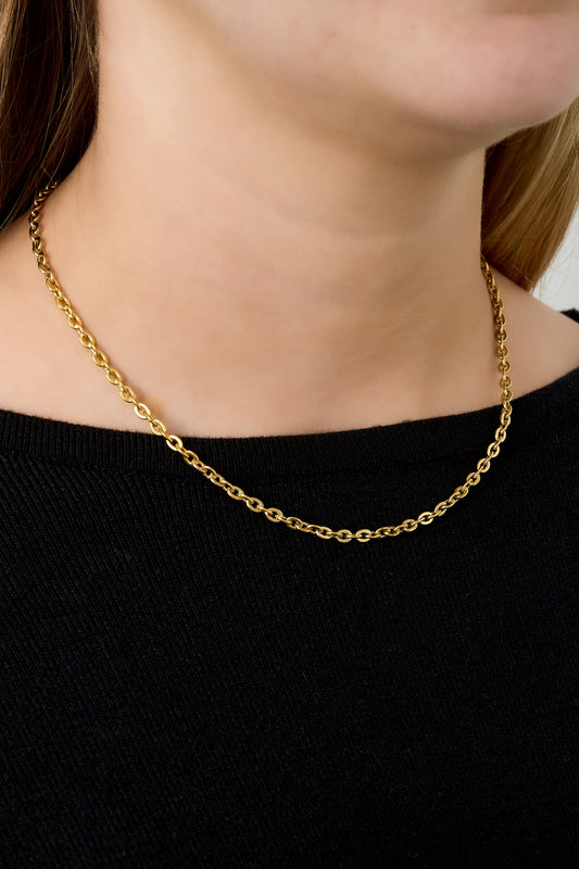 Young woman wearing simple gold chain necklace with black top, showcasing necklace on neck