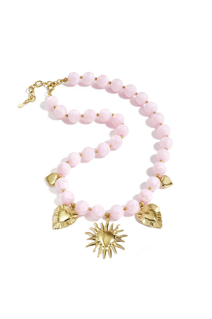 Soft pastel pink beaded necklace with gold heart and sun charms displayed on white background