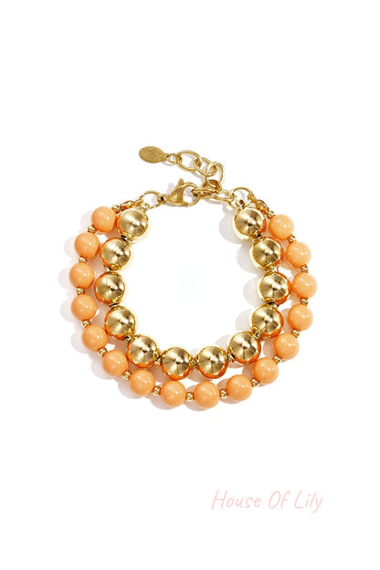 Double layered bracelet with peach acrylic and gold-tone beads on white background