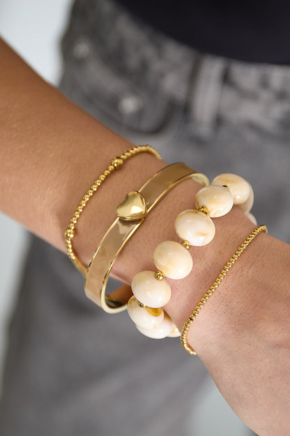 Cream marbled beaded stretch bracelet with gold accent beads worn stacked with other bracelets on woman's wrist