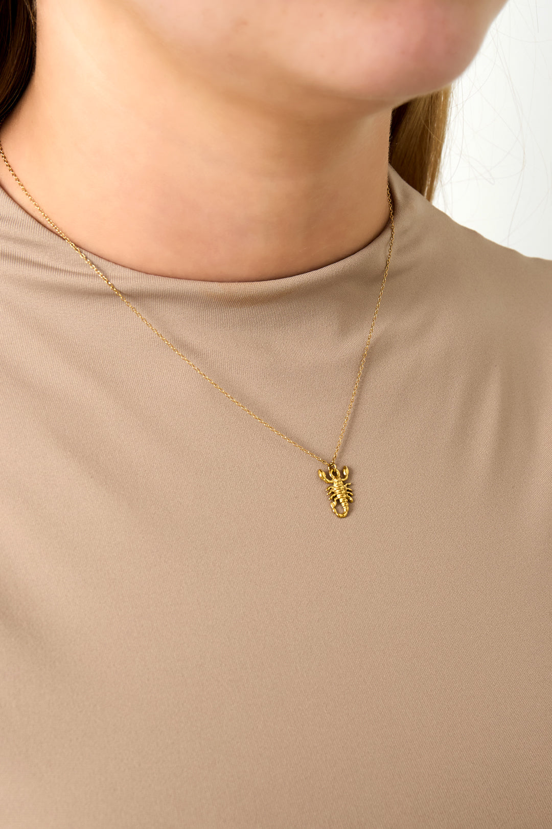 Close-up of woman wearing gold Scorpio scorpion charm necklace with beige top