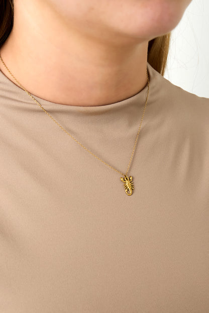Close-up of woman wearing gold Scorpio scorpion charm necklace with beige top