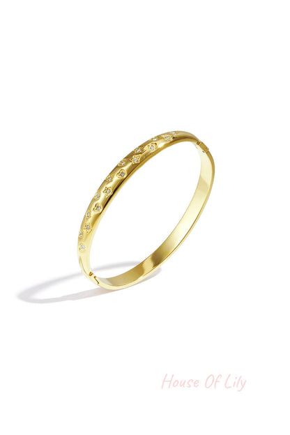 Gold-tone bangle bracelet with star and heart-shaped crystal accents on white background