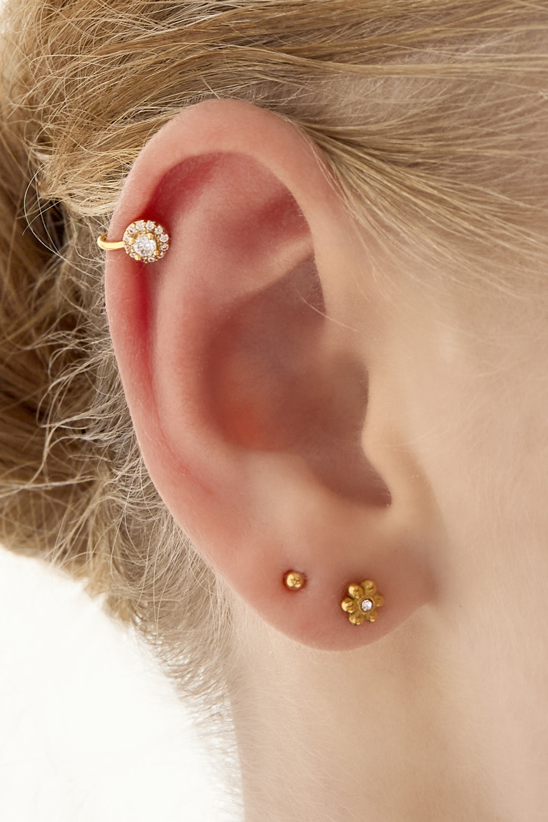 Close-up of an ear with a gold cubic zirconia-studded ear cuff paired with small gold stud earrings