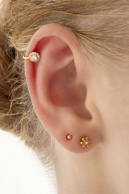 Close-up of an ear with a gold cubic zirconia-studded ear cuff paired with small gold stud earrings
