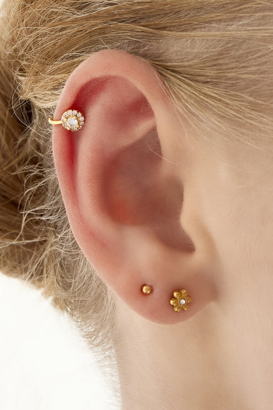 Close-up of an ear with a gold cubic zirconia-studded ear cuff paired with small gold stud earrings