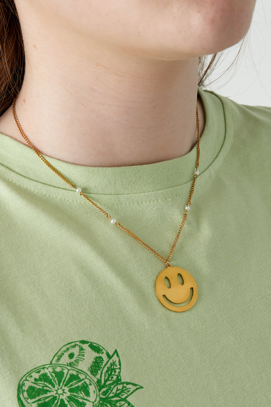 Model wearing the gold smiley face charm necklace with pearl-detailed chain over green shirt