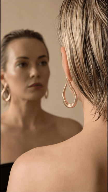 Woman wearing gold hoop earrings looking at herself in a mirror.
