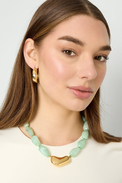 Model wearing mint green chunky beaded necklace with gold centerpiece and gold hoop earrings, showcasing a youthful and minimal aesthetic