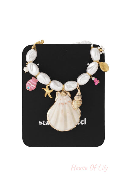 Nautical necklace with white oval pearls, a large seashell charm, and colorful fish and starfish accents on gold chain.