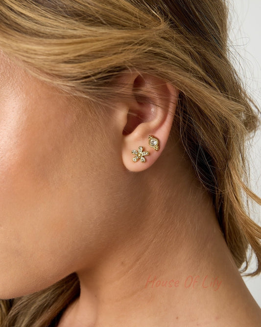 Side profile of woman showing close-up of gold flower stud earrings and small crystal studs on her ear