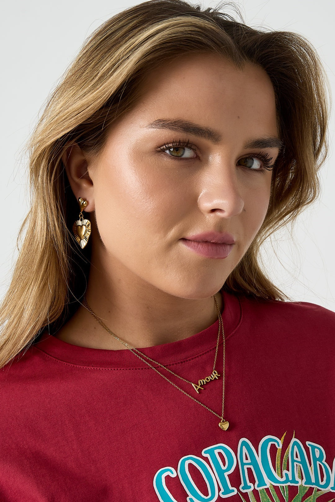 Model wearing gold layered Amour necklace and matching gold heart earrings with red graphic tee