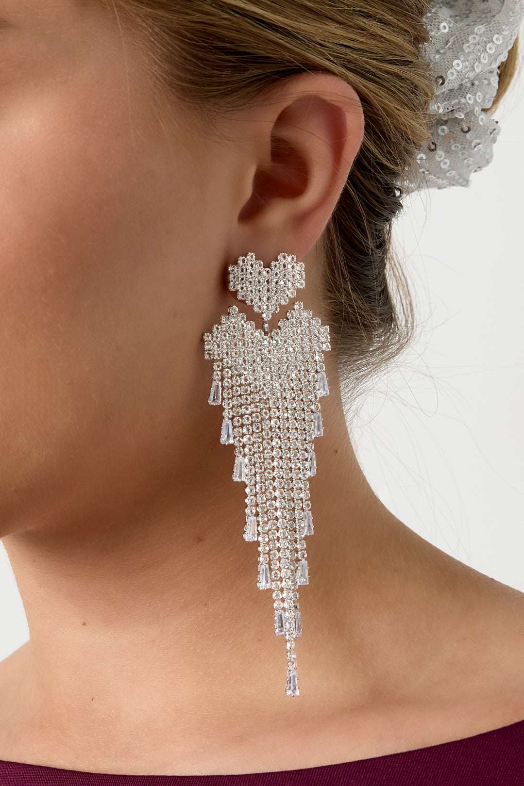 Detailed side view of silver-tone crystal cascade earring showing pixelated heart and fringe on model's ear