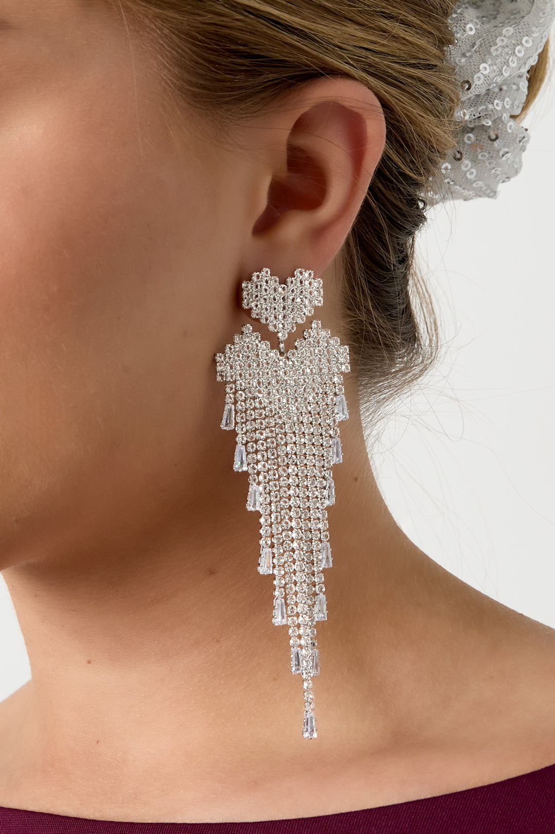 Detailed side view of silver-tone crystal cascade earring showing pixelated heart and fringe on model's ear