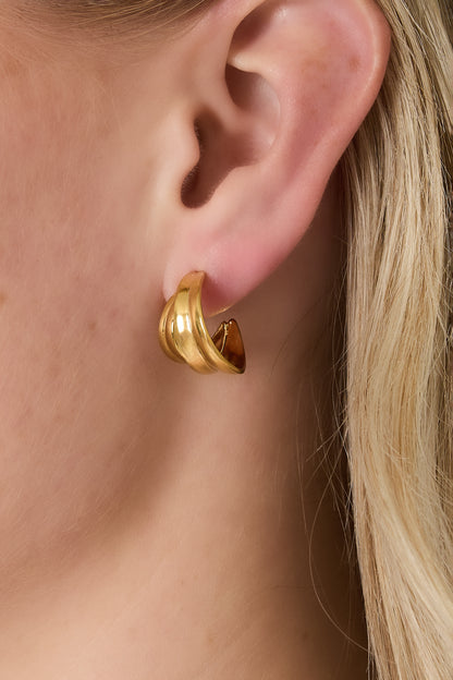 Close-up of a woman wearing the gold sculptural curved hoop earring on her pierced ear, showing fit and style