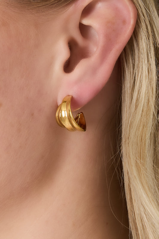 Close-up of a woman wearing the gold sculptural curved hoop earring on her pierced ear, showing fit and style
