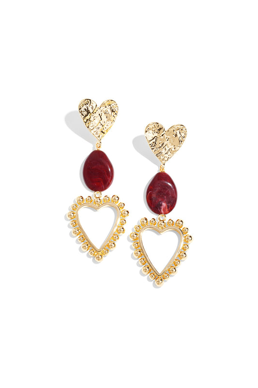 Pair of heart drop statement earrings with hammered gold-tone hearts, crimson red resin bead, and gold beaded open heart frames on white background