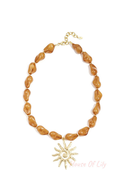 Close-up image of a caramel brown acrylic beaded necklace featuring an artistic gold sun pendant on a white background