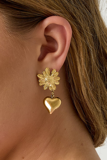 Close-up view of the gold flower heart drop earring on a woman's ear showing detailed flower and glossy heart pendant