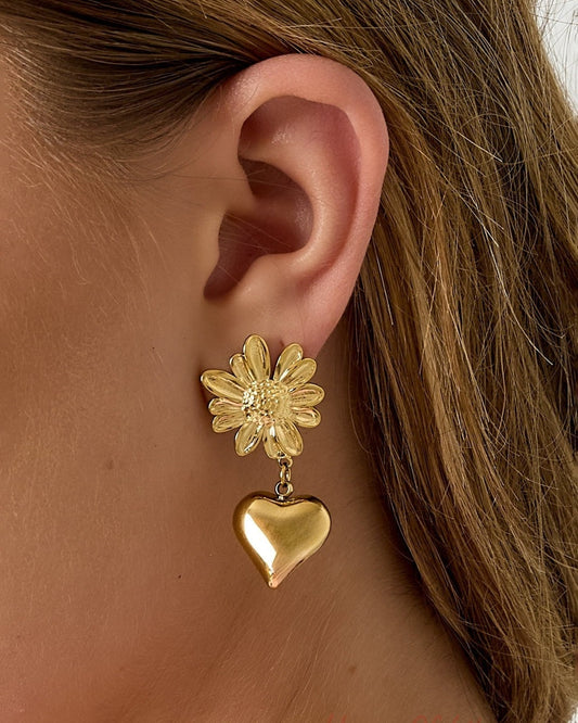 Close-up view of the gold flower heart drop earring on a woman's ear showing detailed flower and glossy heart pendant