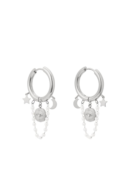 Pair of silver celestial charm hoop earrings with star, moon, sun motifs and pearl chain charms displayed on white background