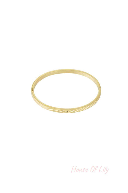 Gold-tone minimal twist metal bangle with hinged clasp on white background