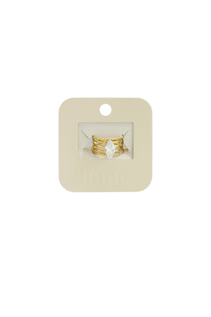 Gold, multi-band statement ring featuring a clear marquise-cut center stone on a branded beige display card.
