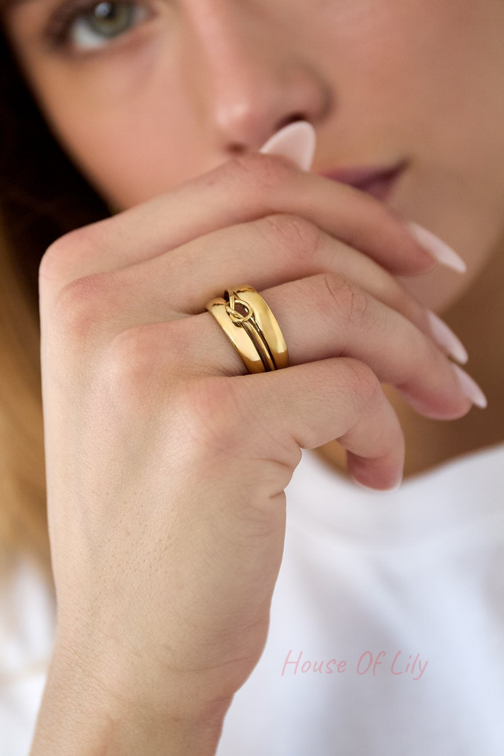 Gold Wavy Gravy ring on a finger, featuring a wide, smooth, polished band with a central delicate knotted design.