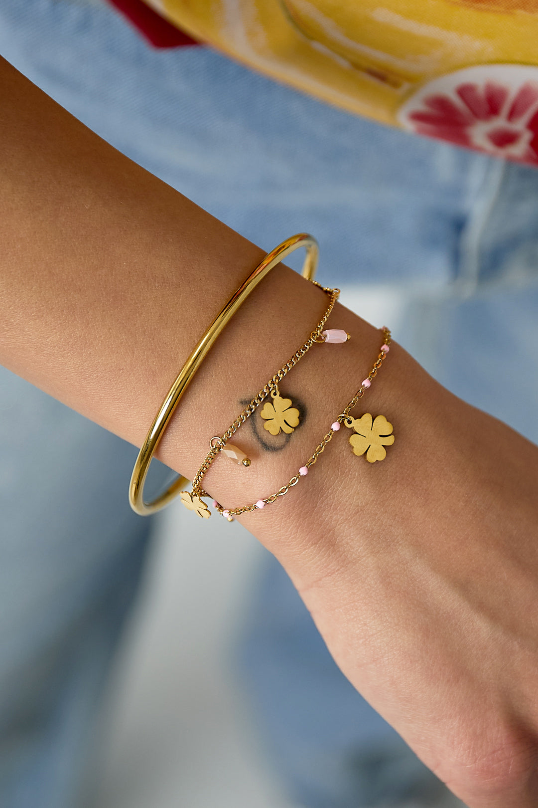 Close-up of a wrist wearing the gold-tone clover charm bracelet alongside a polished gold bangle