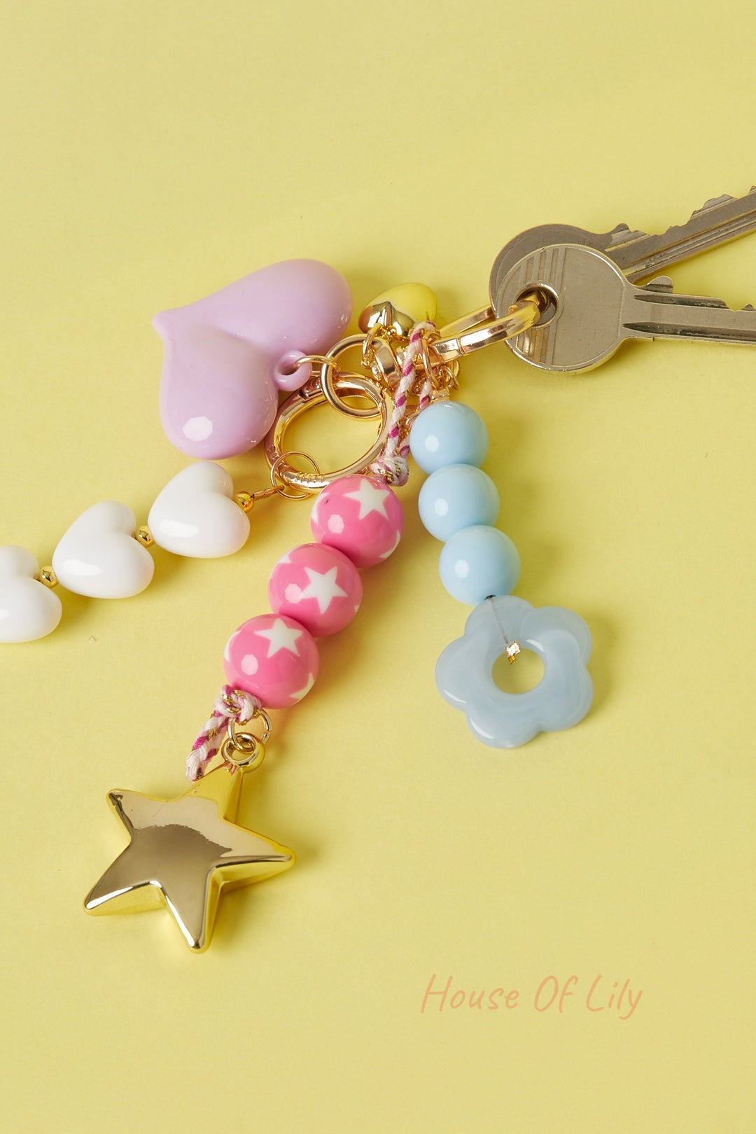 Set of colorful bag charms on keys including pink star bead charm, blue flower charm, and white heart beads on yellow background