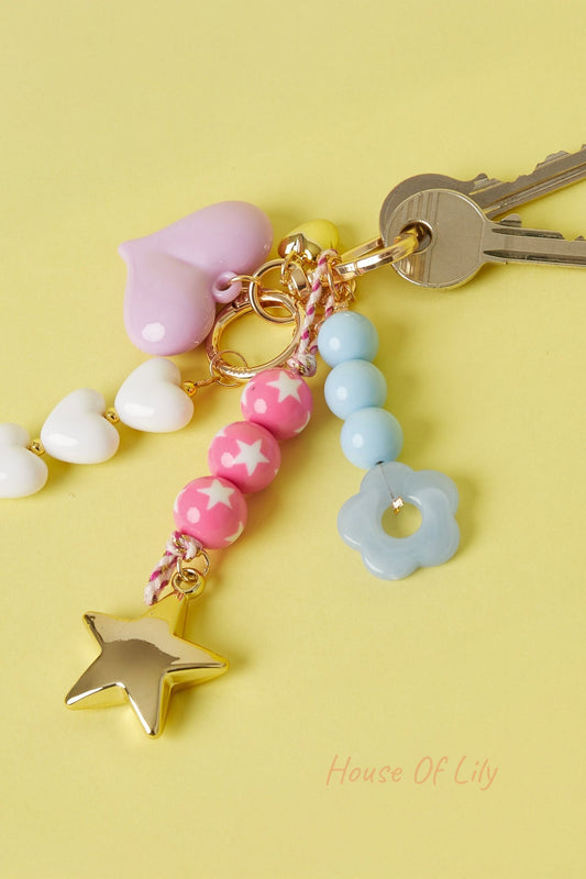 Set of colorful bag charms on keys including pink star bead charm, blue flower charm, and white heart beads on yellow background