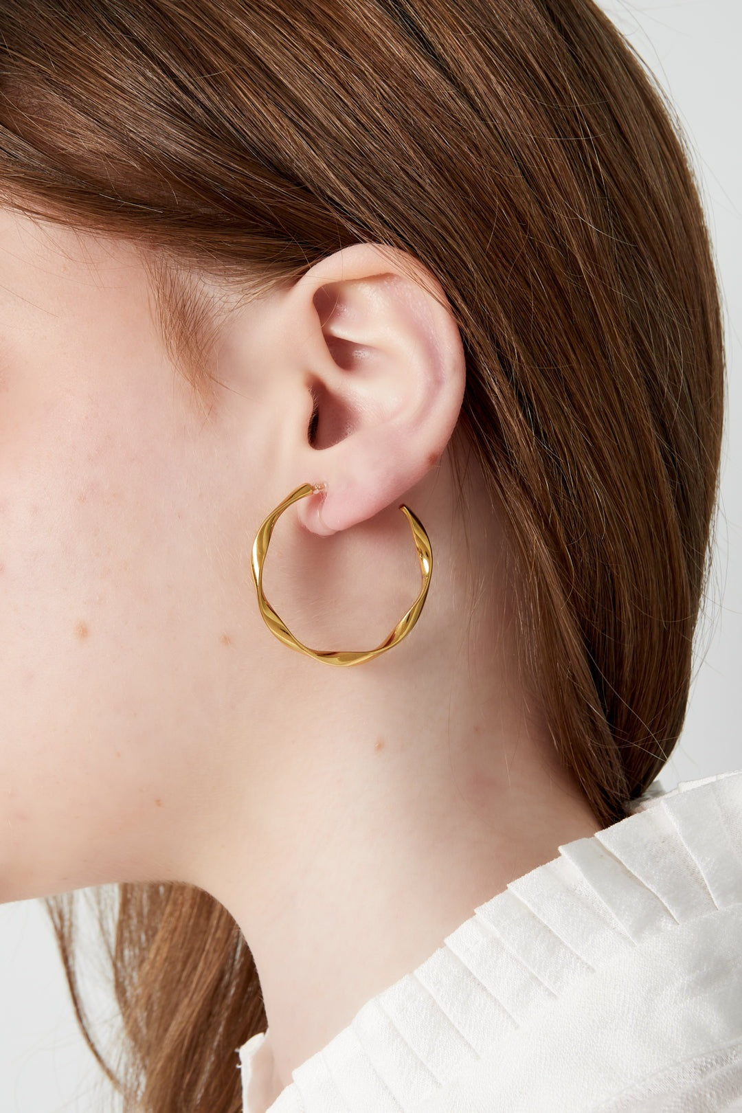 Close-up of a woman wearing a gold-tone twist hoop clip-on earring showing fit and style
