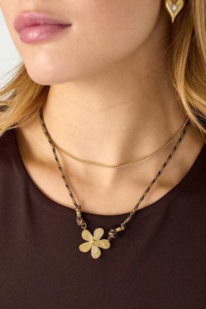 Close-up side view of woman wearing the flower pendant necklace showing layered chains and gold heart-shaped earrings with pearl