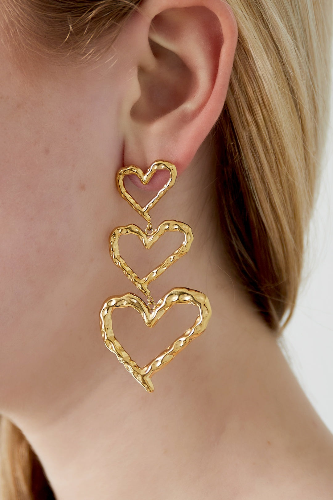Close-up of a woman wearing gold-tone triple heart dangle earrings showing length and playful design