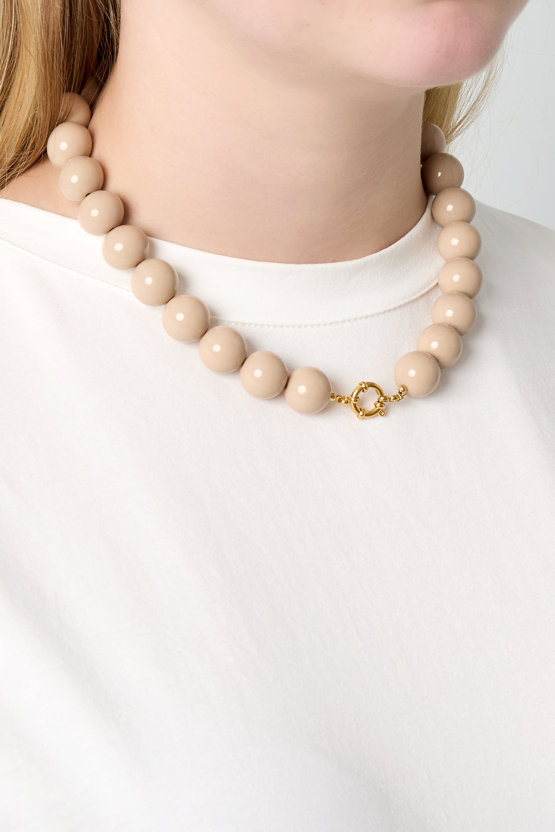 Model wearing beige chunky resin beaded necklace with gold front clasp and white shirt