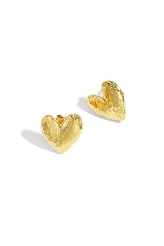 Close-up of gold heart-shaped stud earrings with textured detail placed on white background