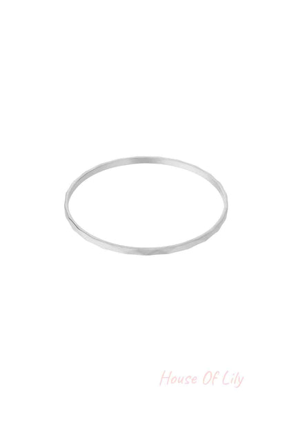 Single thin minimalist hammered silver-tone bangle on white background
