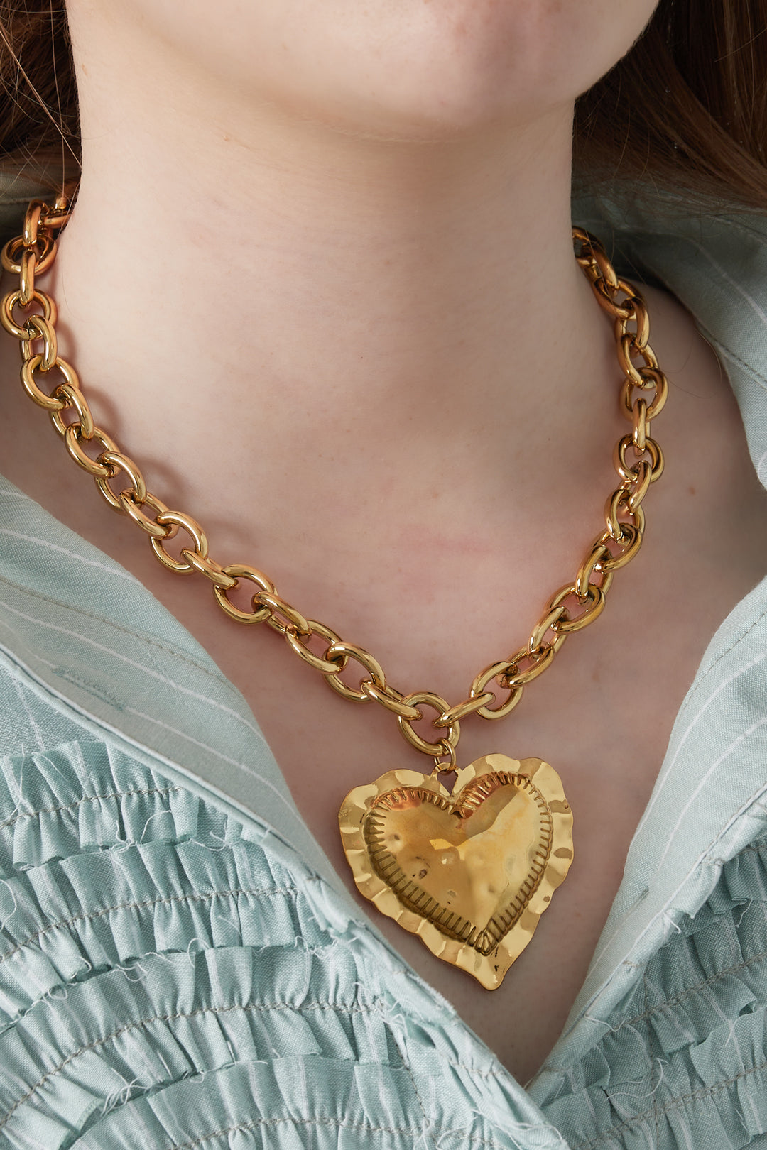 Close-up of woman wearing gold chunky heart pendant necklace over a green ruched top