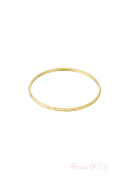 Gold slender minimalist bangle bracelet with subtle starburst engraving on a white background