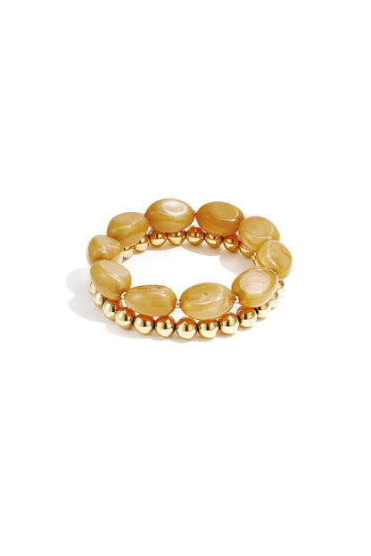 Close-up of two beaded stretch bracelets featuring oval honey-toned resin beads and gold-tone round beads on white background