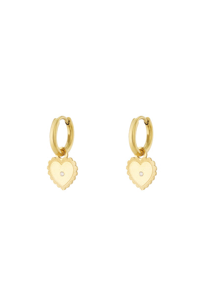 Gold hoop earrings with dangling heart charm featuring central rhinestone on white background
