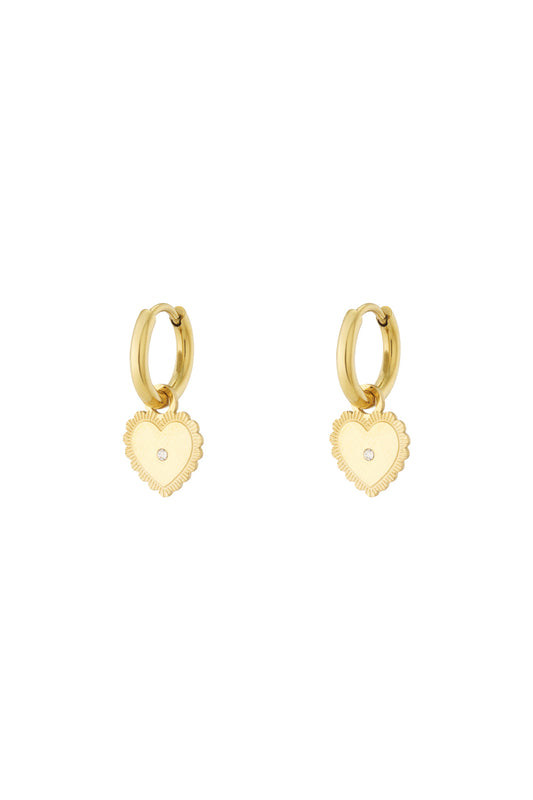 Gold hoop earrings with dangling heart charm featuring central rhinestone on white background